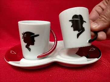 Cette photo montre un service à café duo (2 tasses sur un plateau) décoré en noir et rouge avec une tête de femme et un tête d'homme 
